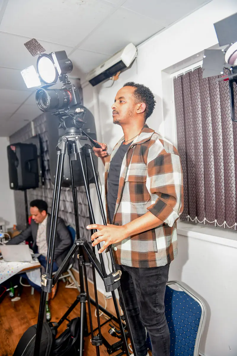 Man adjusting a video camera on a tripod indoors during a filming setup.